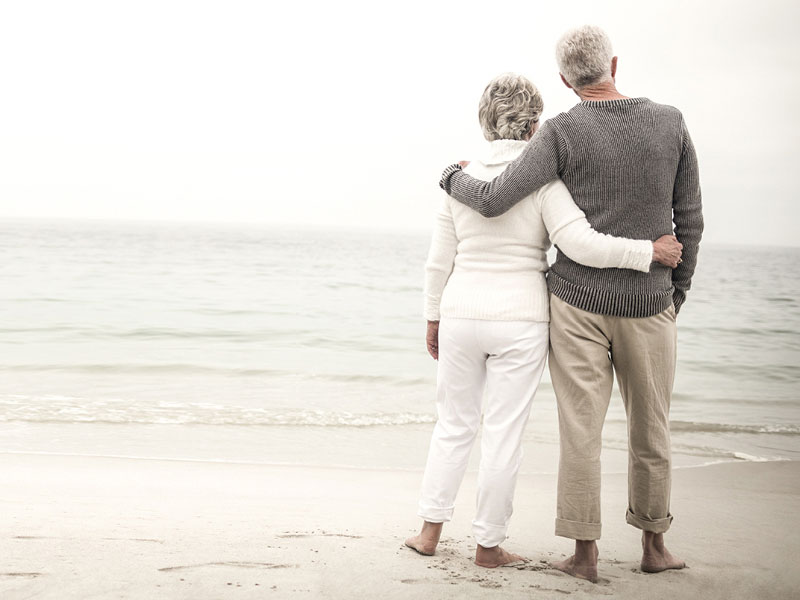 ein älteres Paar steht dem Meer zugewandt am Strand